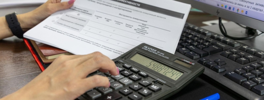 Person calculating project costs using a calculator and financial documents at a desk