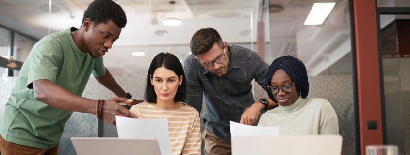 Cross-functional business team discussing planning documents and laptops during an office meeting