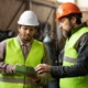 Two manufacturing professionals in safety vests and hard hats reviewing operations at an industrial facility